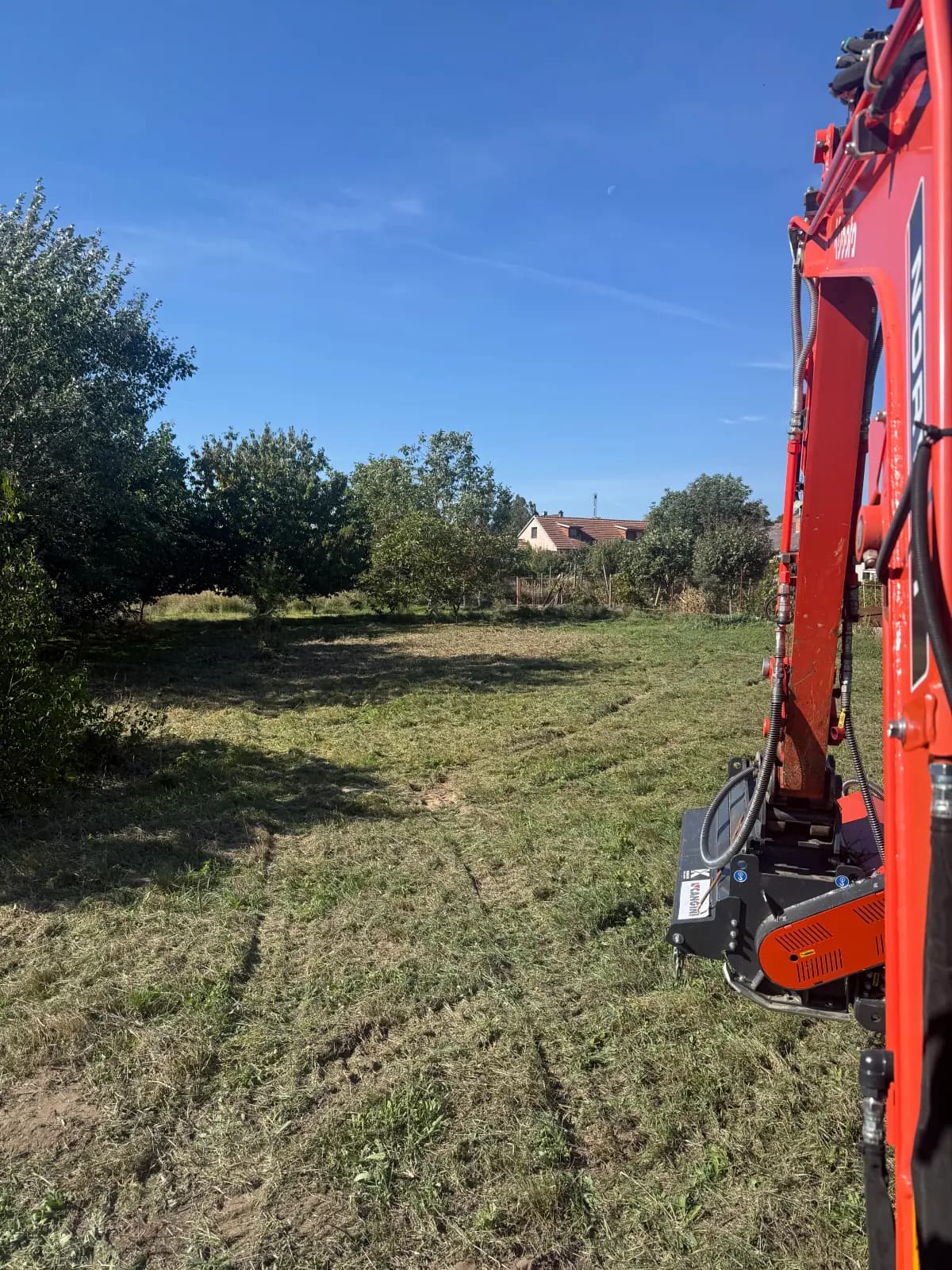 Pomulčovaná plocha s nízkym porastom a ramenom minibagra v Malackách